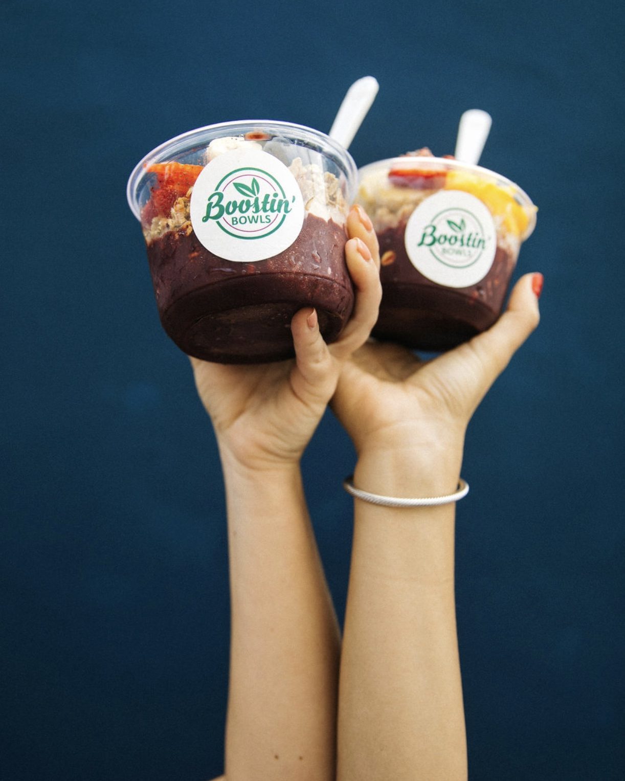 Two açaí bowls held up against a blue wall