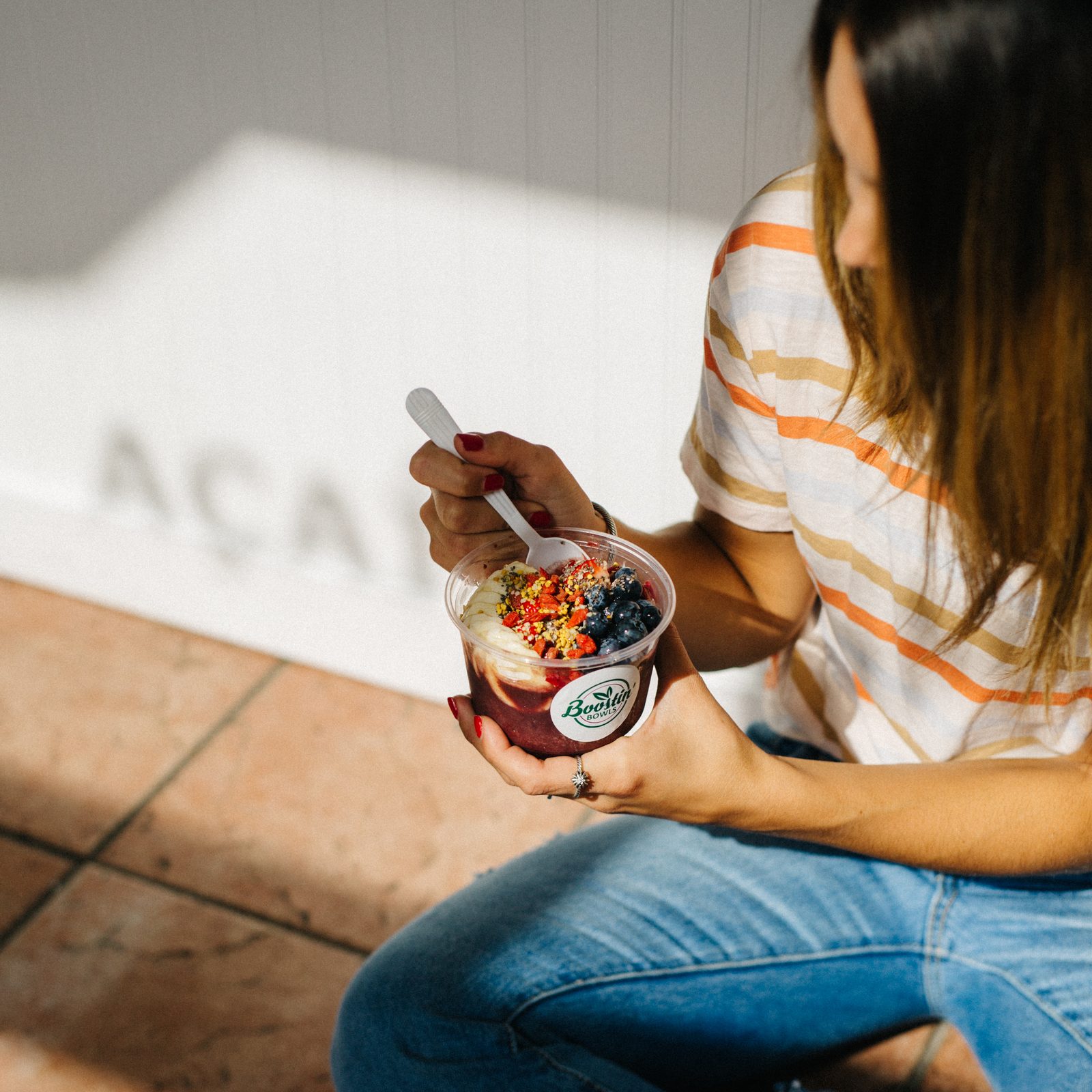 Jenna sitting on a tiled floor holding an açaí bowl