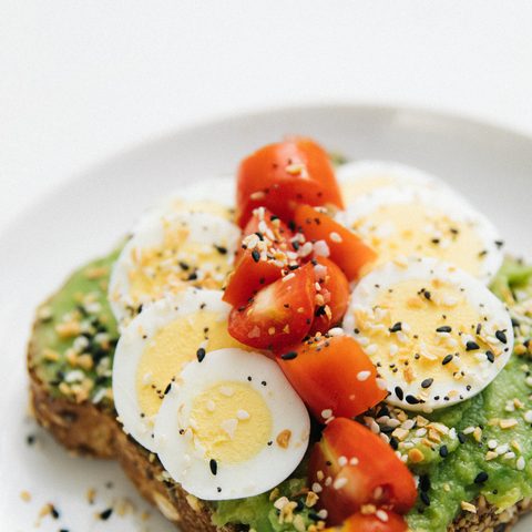 Avocado toast topped with sliced egg, tomatoes and seeds