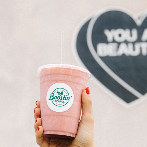 A strawberry banana smoothie held up in a Boostin' Bowls cup