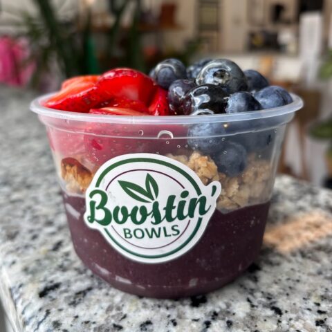Deep purple bowl with granola, blueberries, strawberries, and honey drizzle